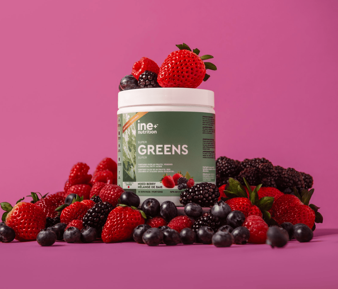 A container of ine+ nutrition Super Greens powder, Mixed Bery with strawberry, raspberries, blackberries and blueberry fruits in the background.